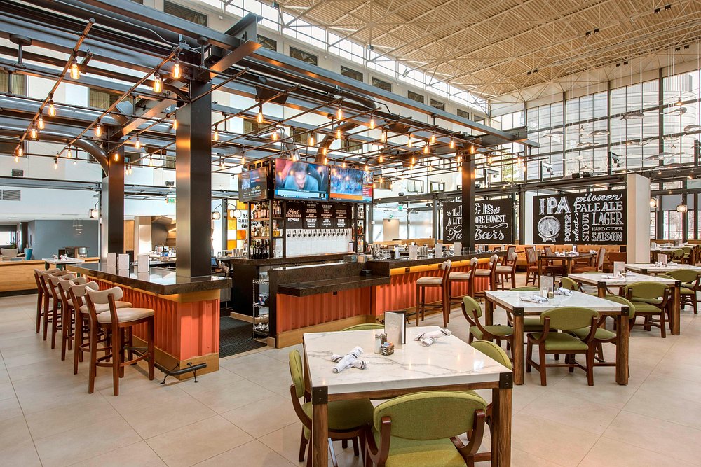 Bar inside hotel with red tables on the side and brown high top chairs at the bar