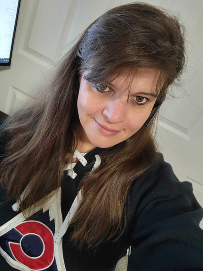 Brenda, long brown hair with swopped bangs, smiling and has on a blue Avalanche hoodie