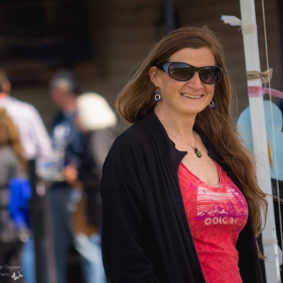 Becky, a smiling redhead in sunglasses, a black jacket and redish pink low cut colorado tshirt outside